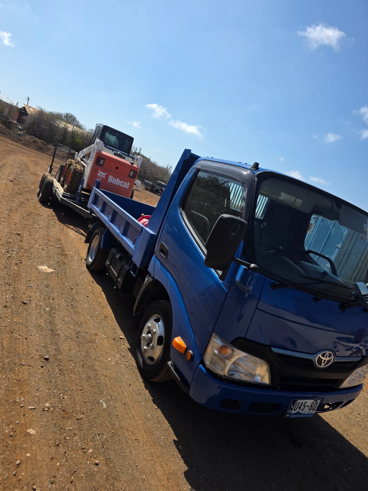 Blue JDS truck transporting a Bobcat in Curaçao