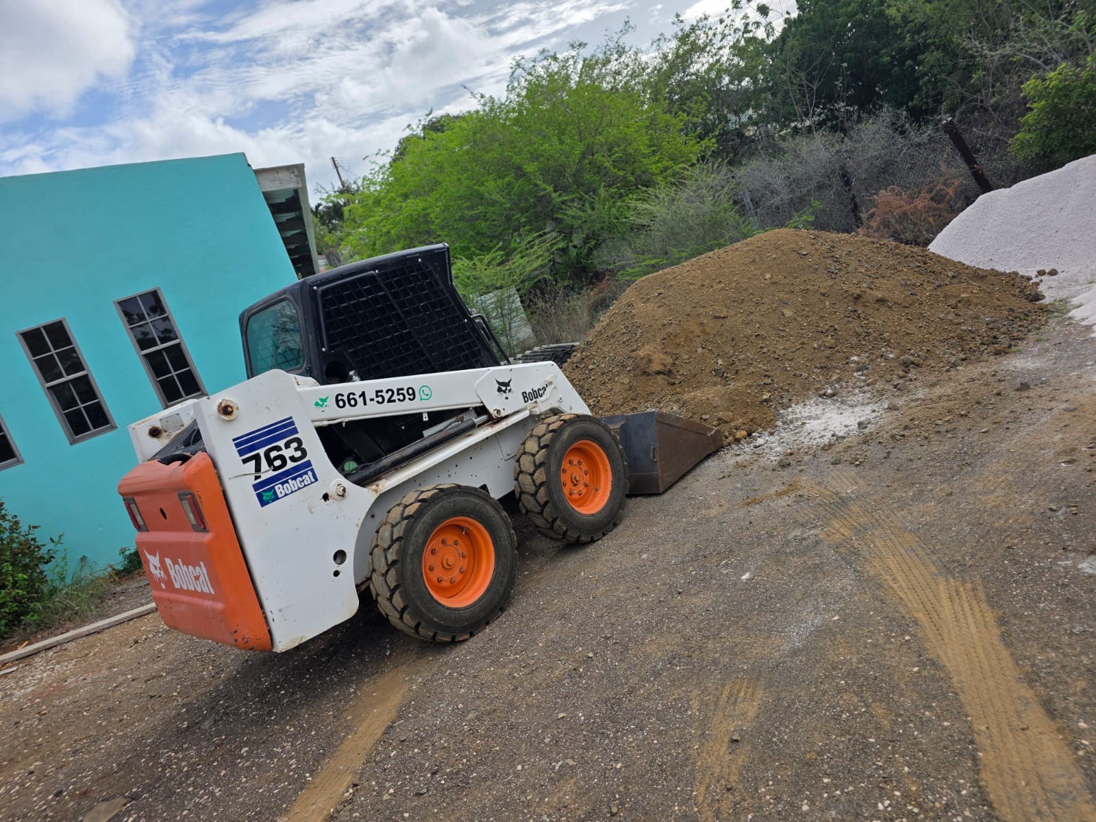 JDS Bobcat preparing ground beside piles of construction material